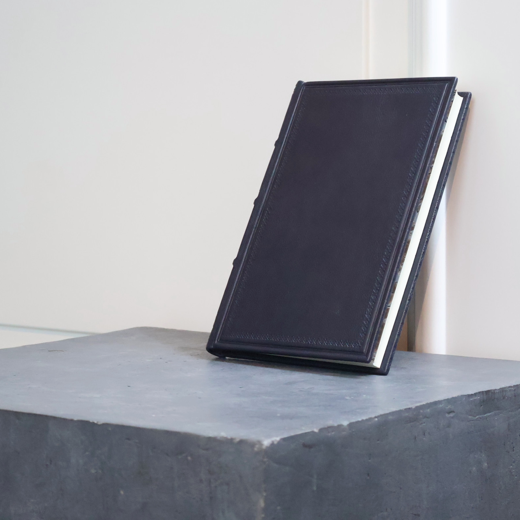 A navy blue Achilleis leather-bound book leaning against the wall, with its spine visible between the bookends